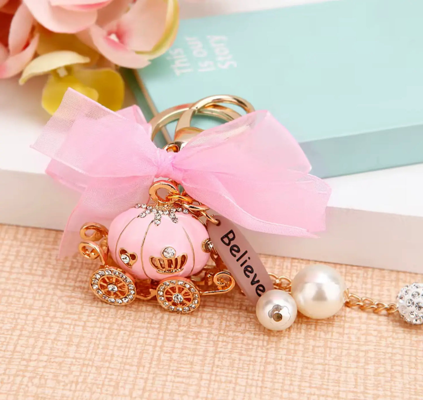Keychain with pink pumpkin, bow, and 'Believe' ribbon on a textured surface