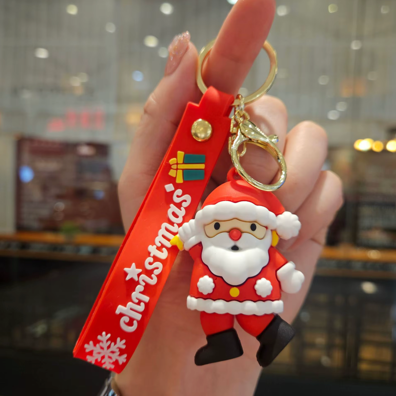 Santa Claus keychain with 'Christmas' strap held by a hand against a blurred indoor background