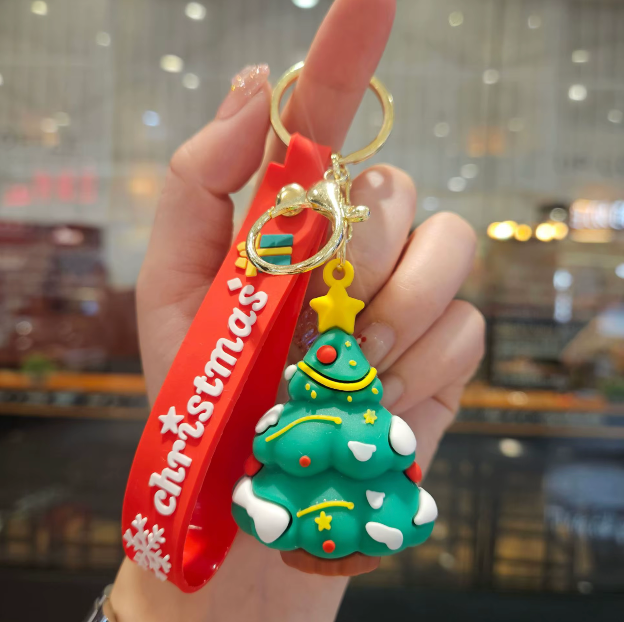 Hand holding a Christmas tree keychain with a red ribbon and gold accents.