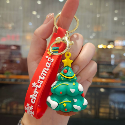 Hand holding a Christmas tree keychain with a red ribbon and gold accents.