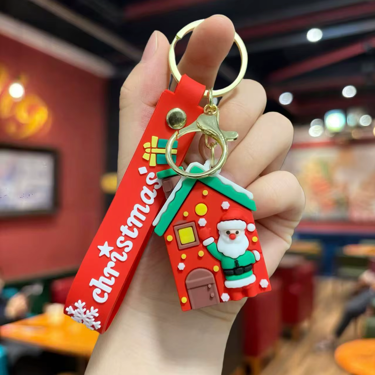 Hand holding a Christmas-themed keychain with a red house design and Santa Claus figure.