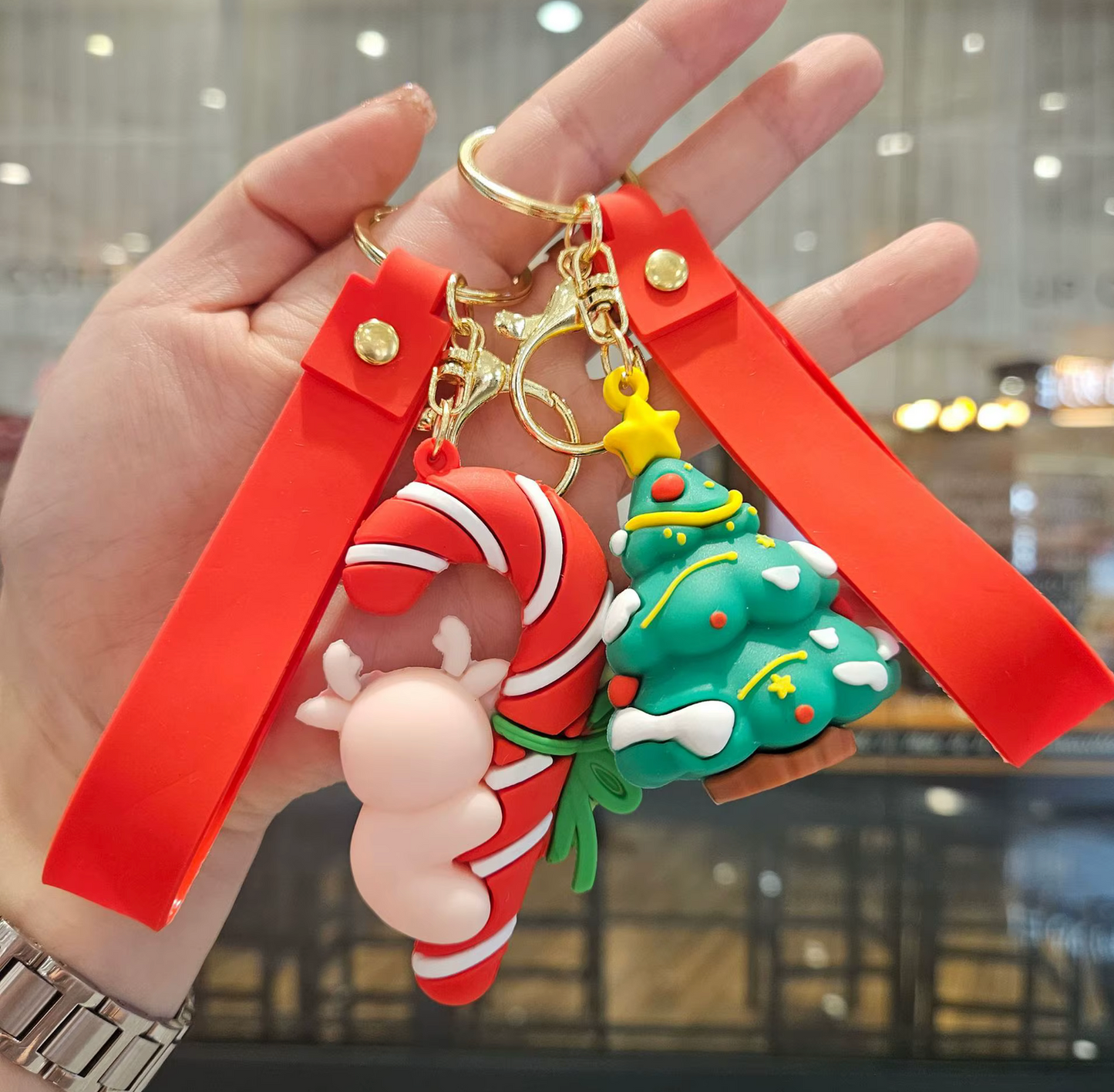 Keychain with Christmas-themed charms including a candy cane, reindeer, and Christmas tree held by a hand.