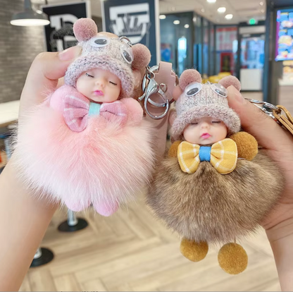 Two fluffy keychains shaped like cartoon characters held in a hand with a blurred indoor background.