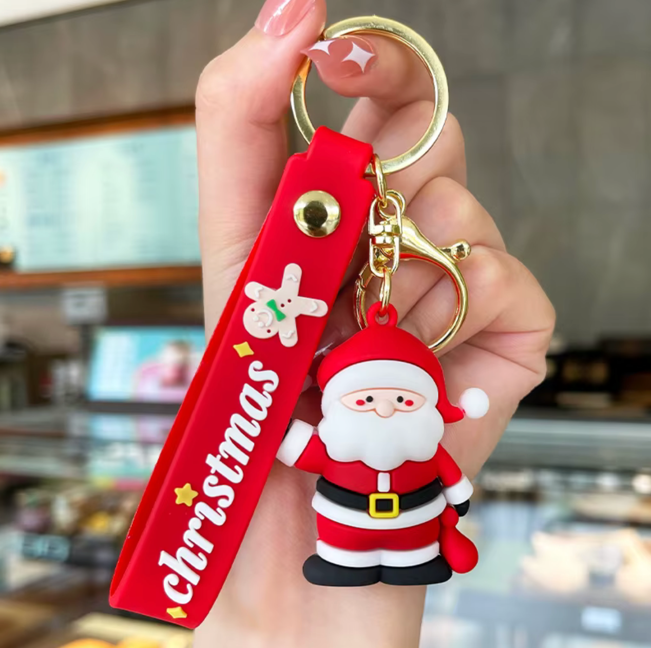 Keychain with Santa Claus figure and 'Christmas' tag held by a hand in a blurred indoor setting