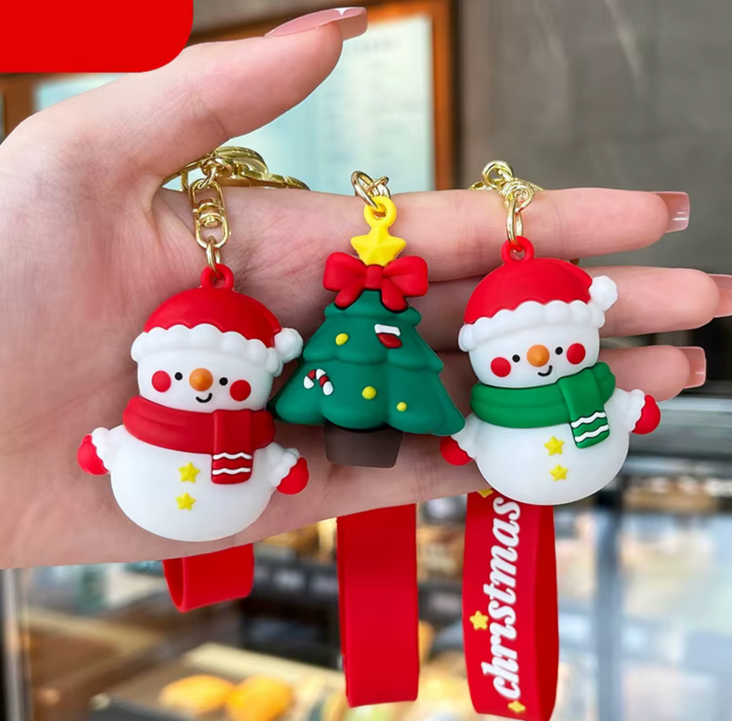 Hand holding three Christmas-themed keychains: a snowman, a tree, and a Santa Claus figure.