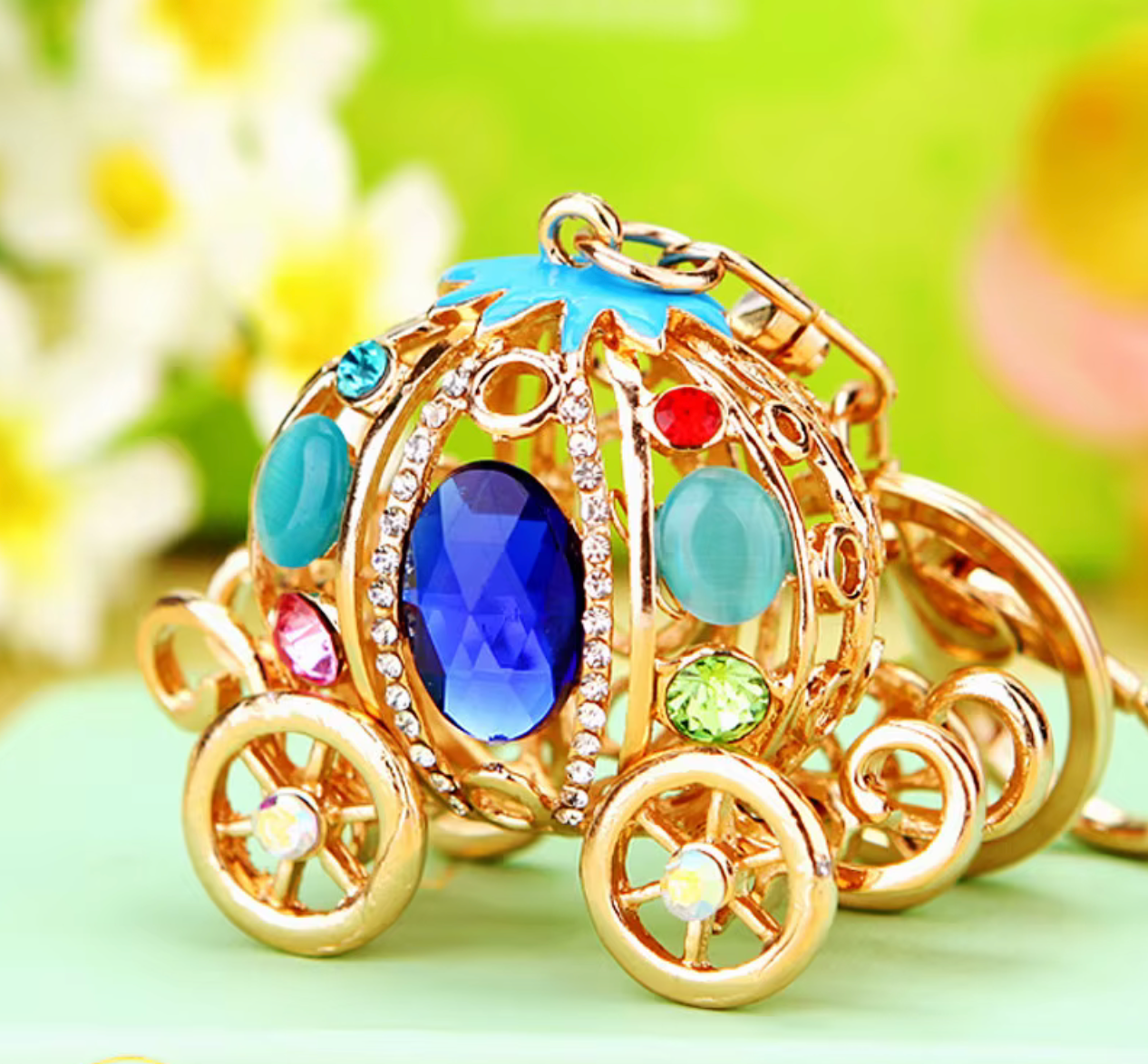 Decorative keychain shaped like a gold carriage with colorful gemstones on a green background