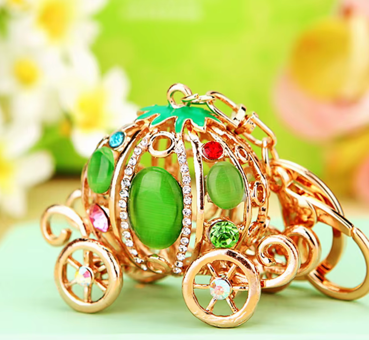 Gold-colored carriage charm with green and red stones on a light green background