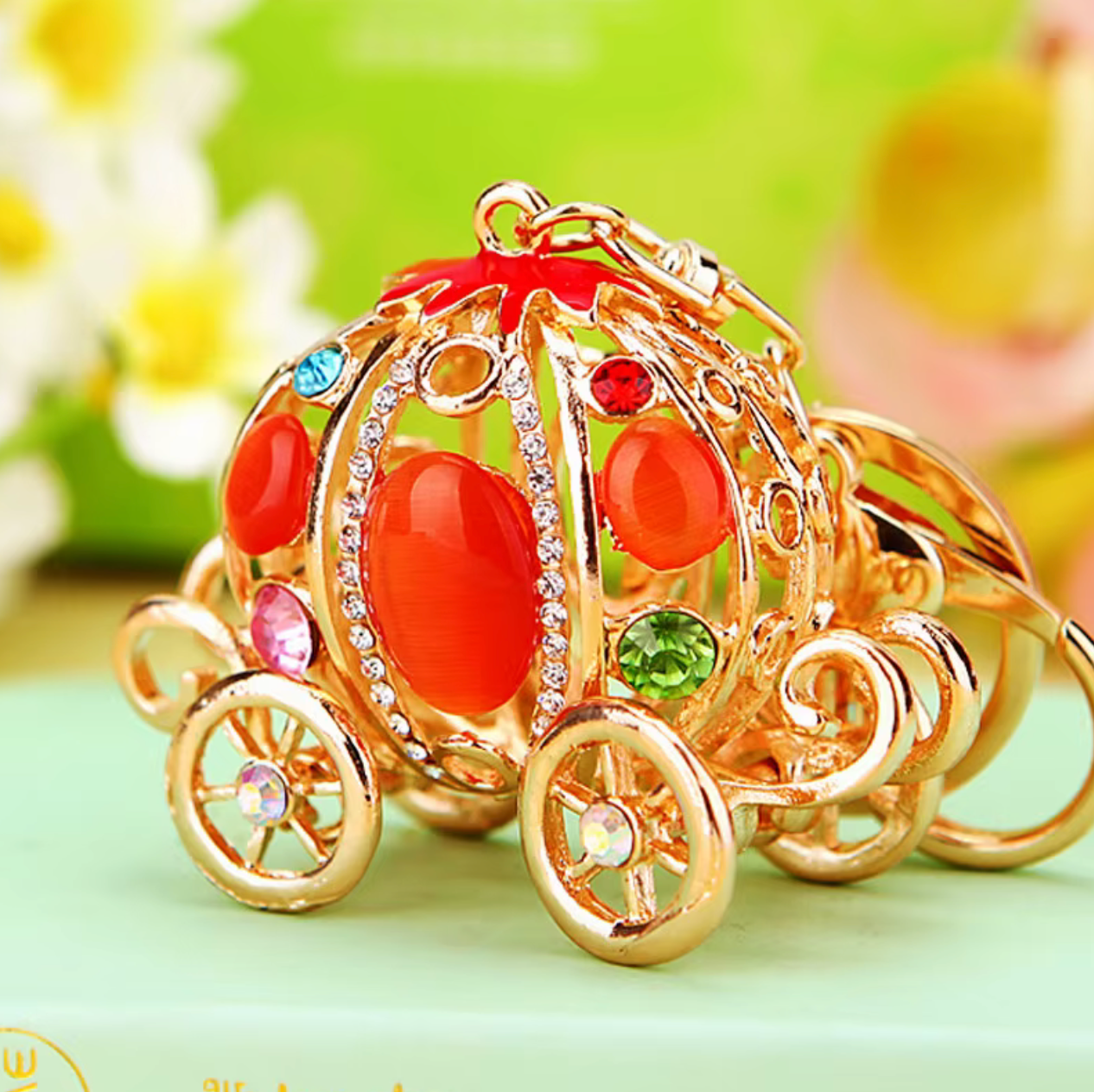 Gold car keychain with red and gemstone accents on a light green background