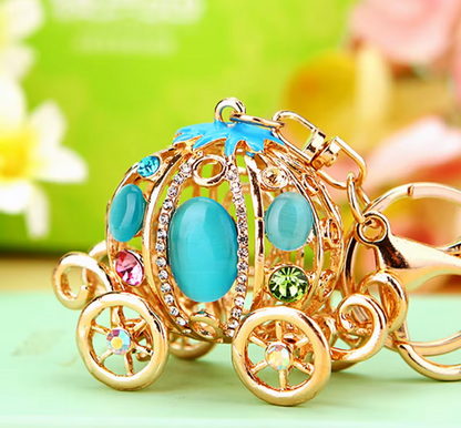 Gold car-shaped keychain with blue and pink stones on a green background