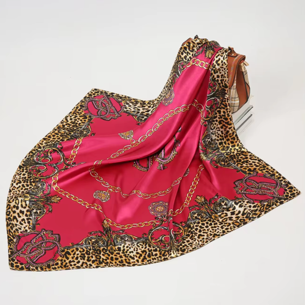 Pink scarf with leopard print and chain pattern draped over a handbag on a white background